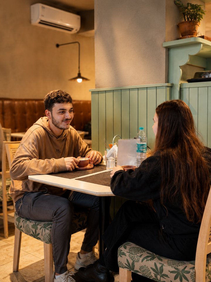 Two friends talking over coffee in a green-panelled corner of Café Vagabond