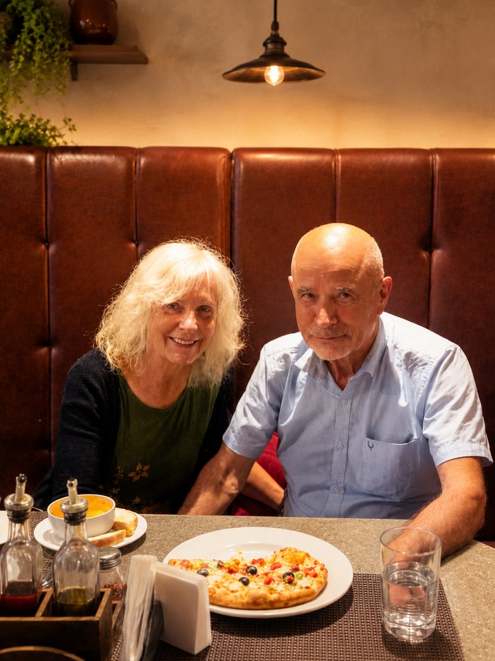 A couple sharing a pizza and soup in a leather booth at Café Vagabond